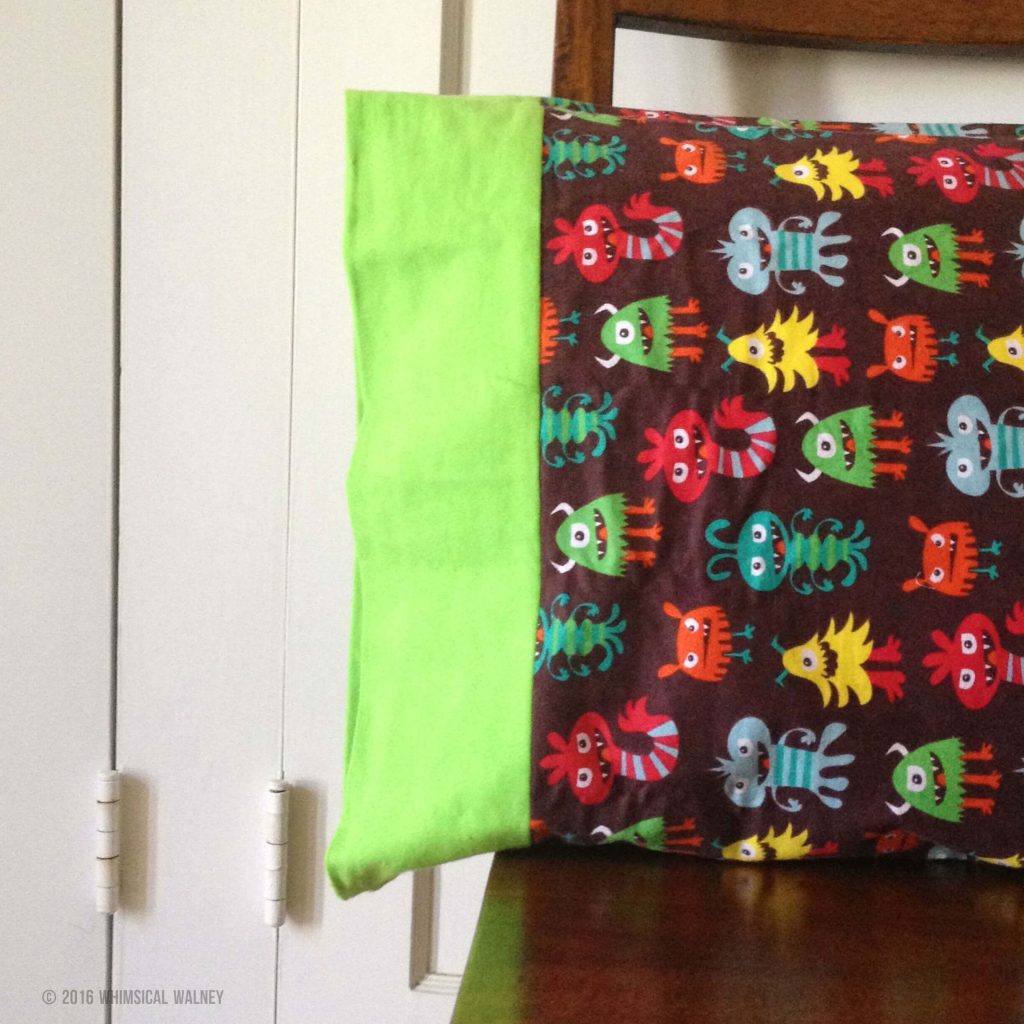Handmade flannel pillowcase set on a wood chair. The main fabric is goofy, colorful monsters on a background and the border is a bright, almost neon green.