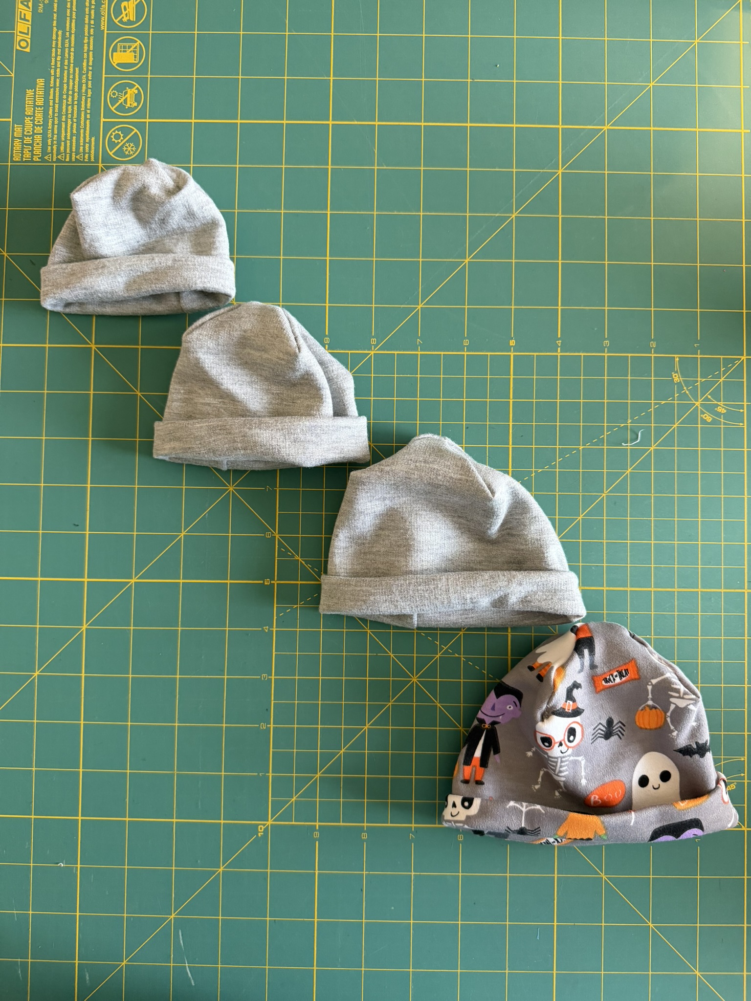 Preemie hats laid out in four different sizes on a green cutting mat.