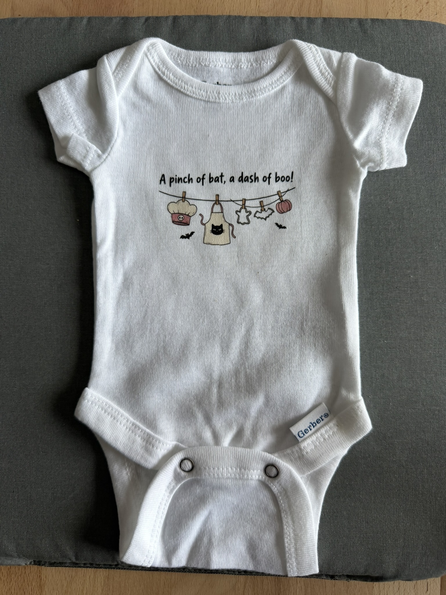 White preemie bodysuit with a cute Halloween-themed design on a gray pressing mat.