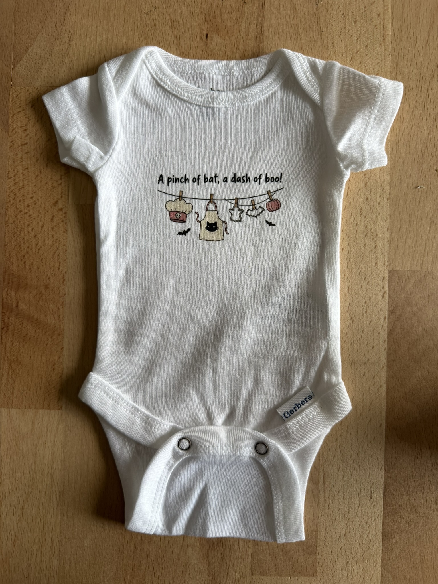 Preemie bodysuit on a wood table with a cute Halloween graphic as part of Preemies of the Carolinas Boo in the NICU.
