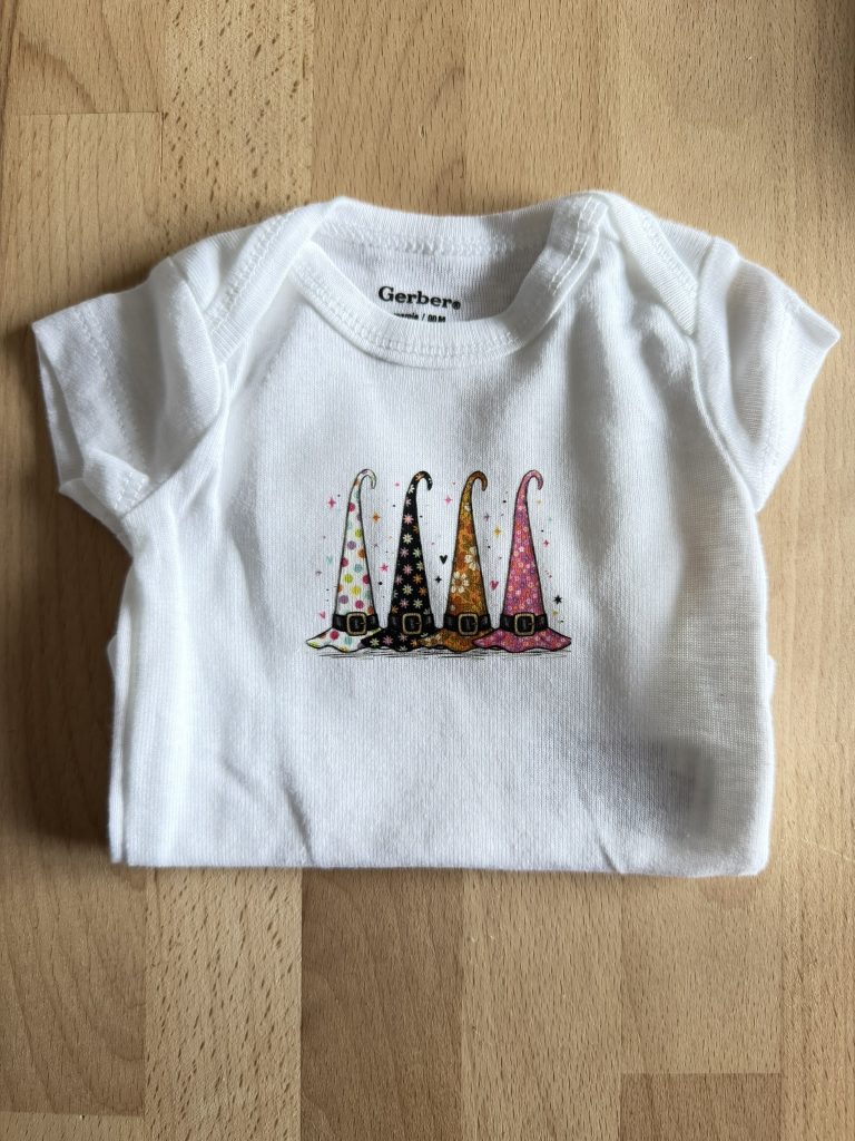 White preemie-sized onesie with colorful witch's hats.