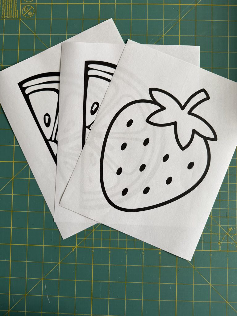 Line drawing of a strawberry of a white piece of paper laid out with other designs on a green cutting mat.