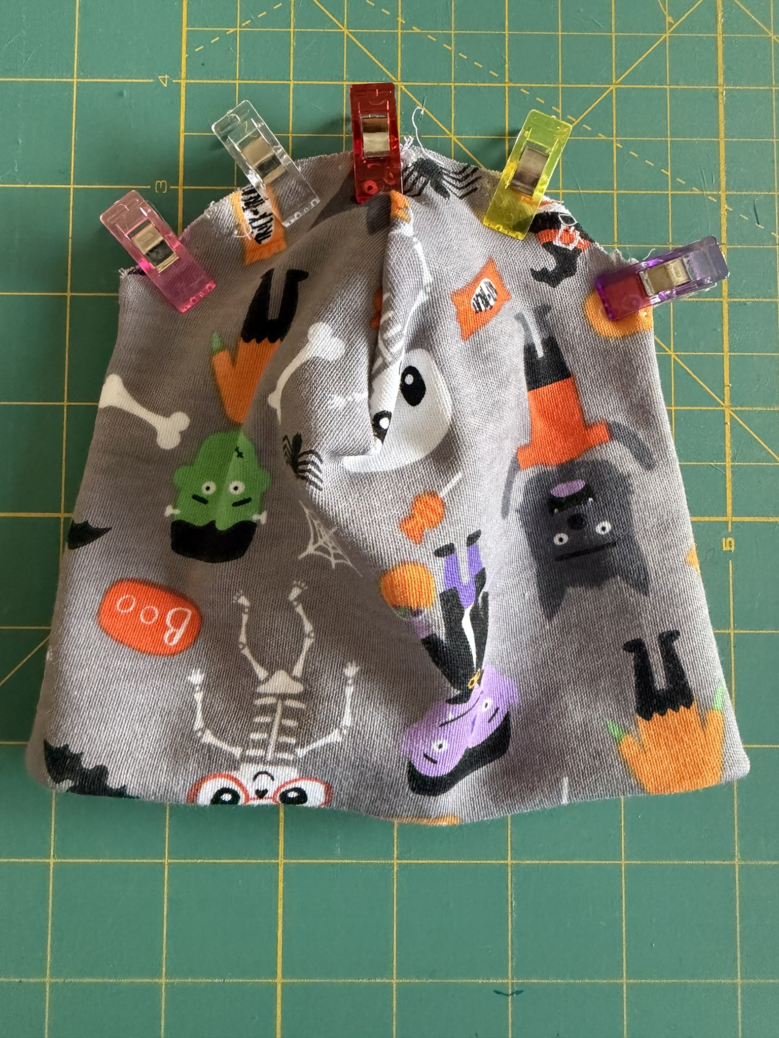 Halloween-themed knit fabric clipped together to sew the top seam oa preemie hat.