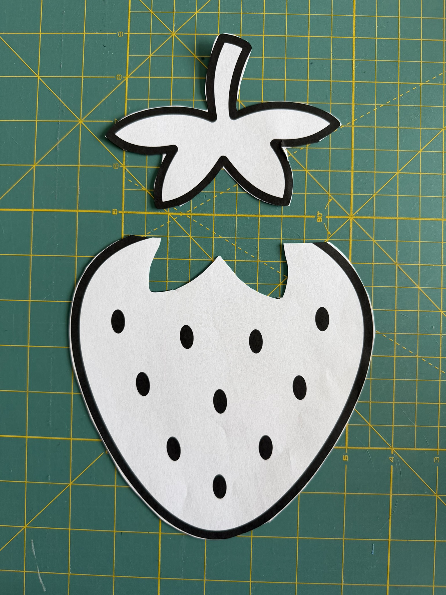 Strawberry paper template cut into two pieces placed on a green cutting mat.