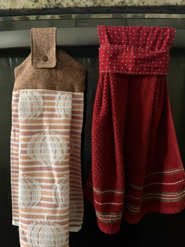 Two styles of hanging kitchen towels displayed on the handle of a dishwasher.