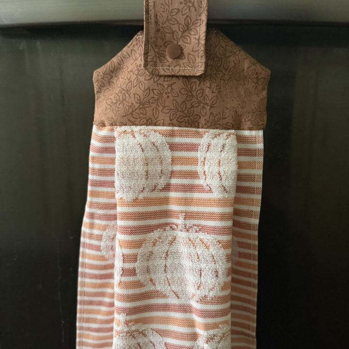 Fall-themed hanging dish towel hanging from the handle of a dishwasher.