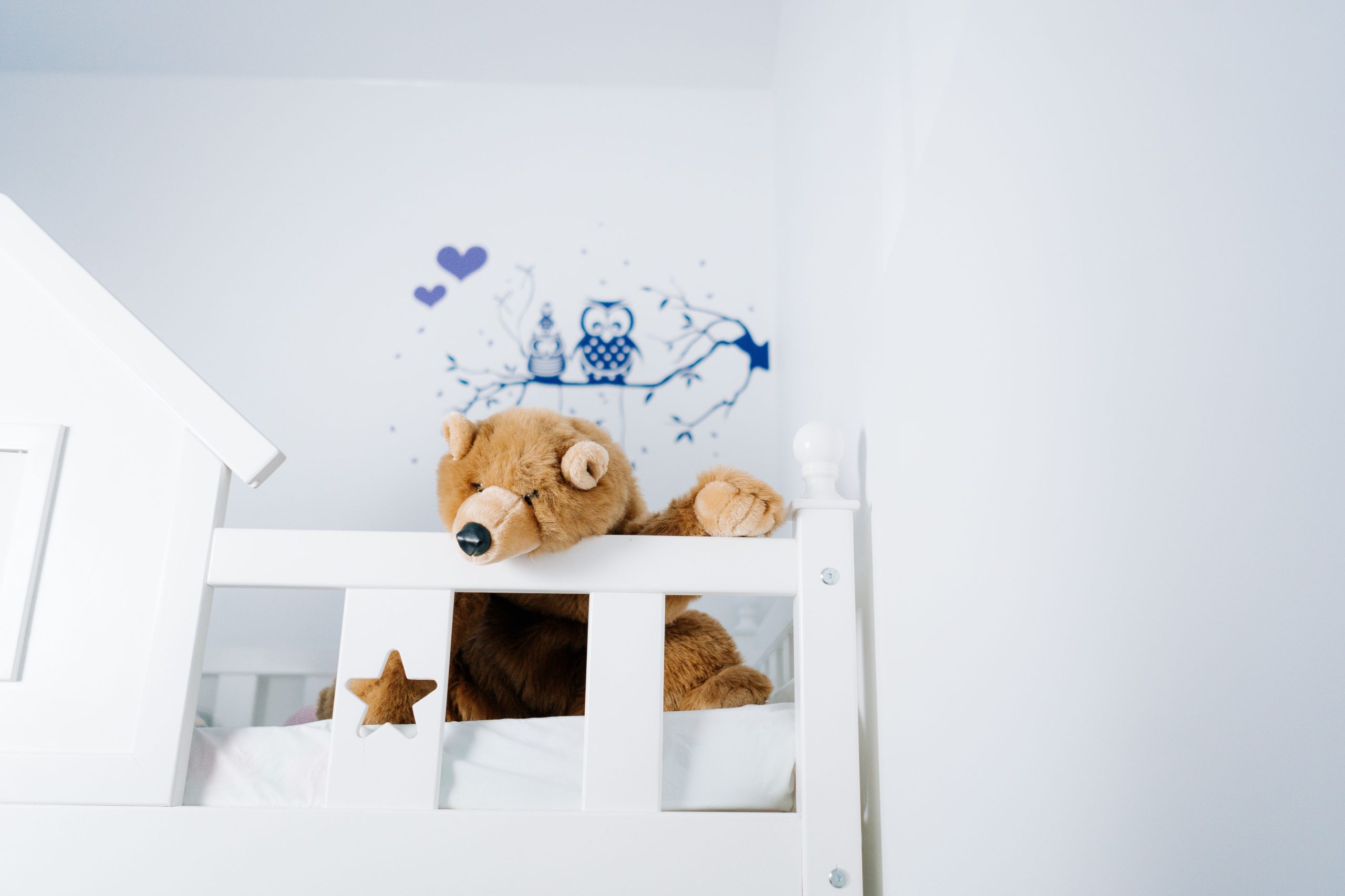 A large, brown stuffed beat on the top of a white bunk bed.
