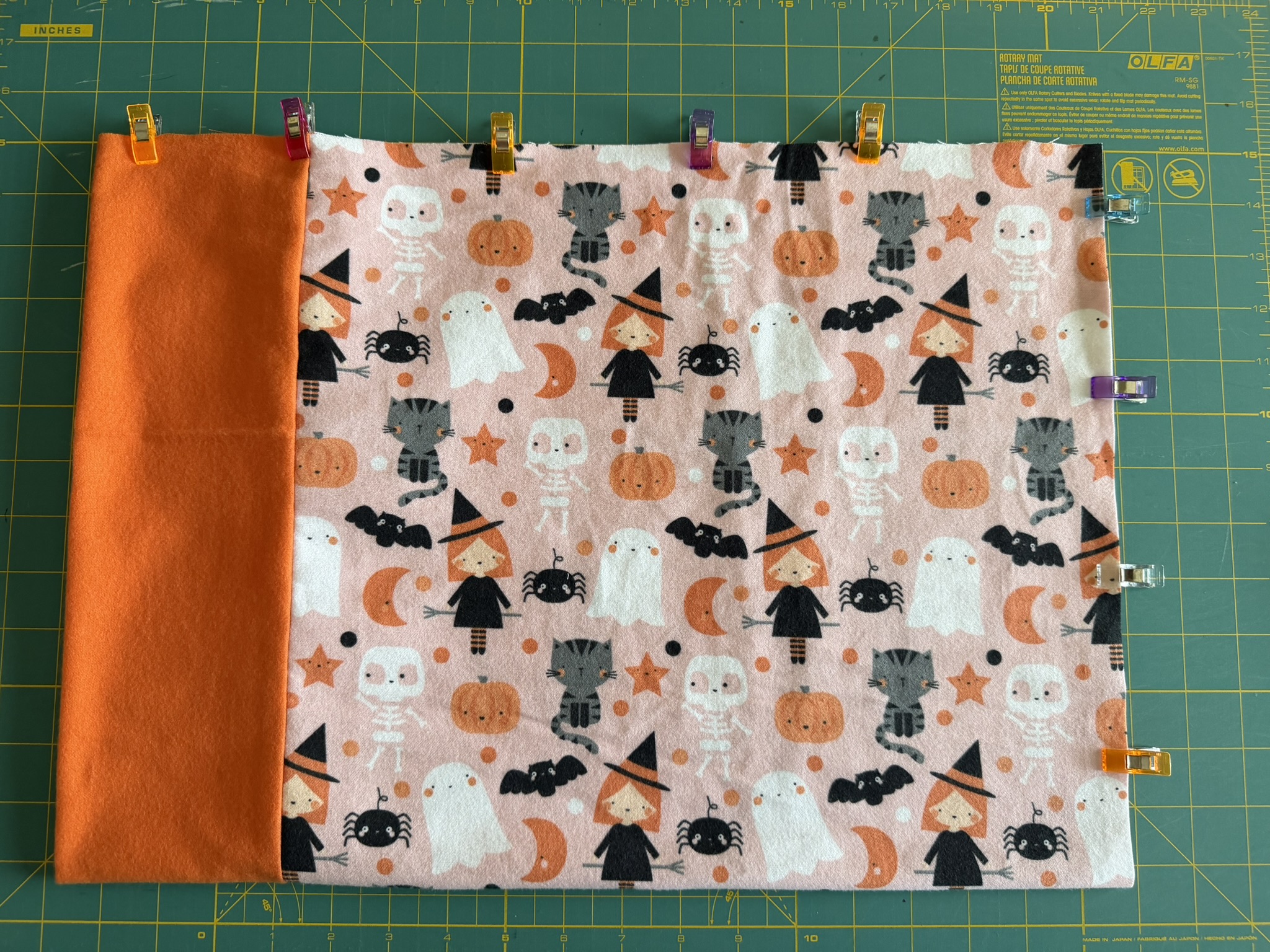 Halloween-themed fabric with an orange border clipped together to prepare for sewing a toddler pillowcase.