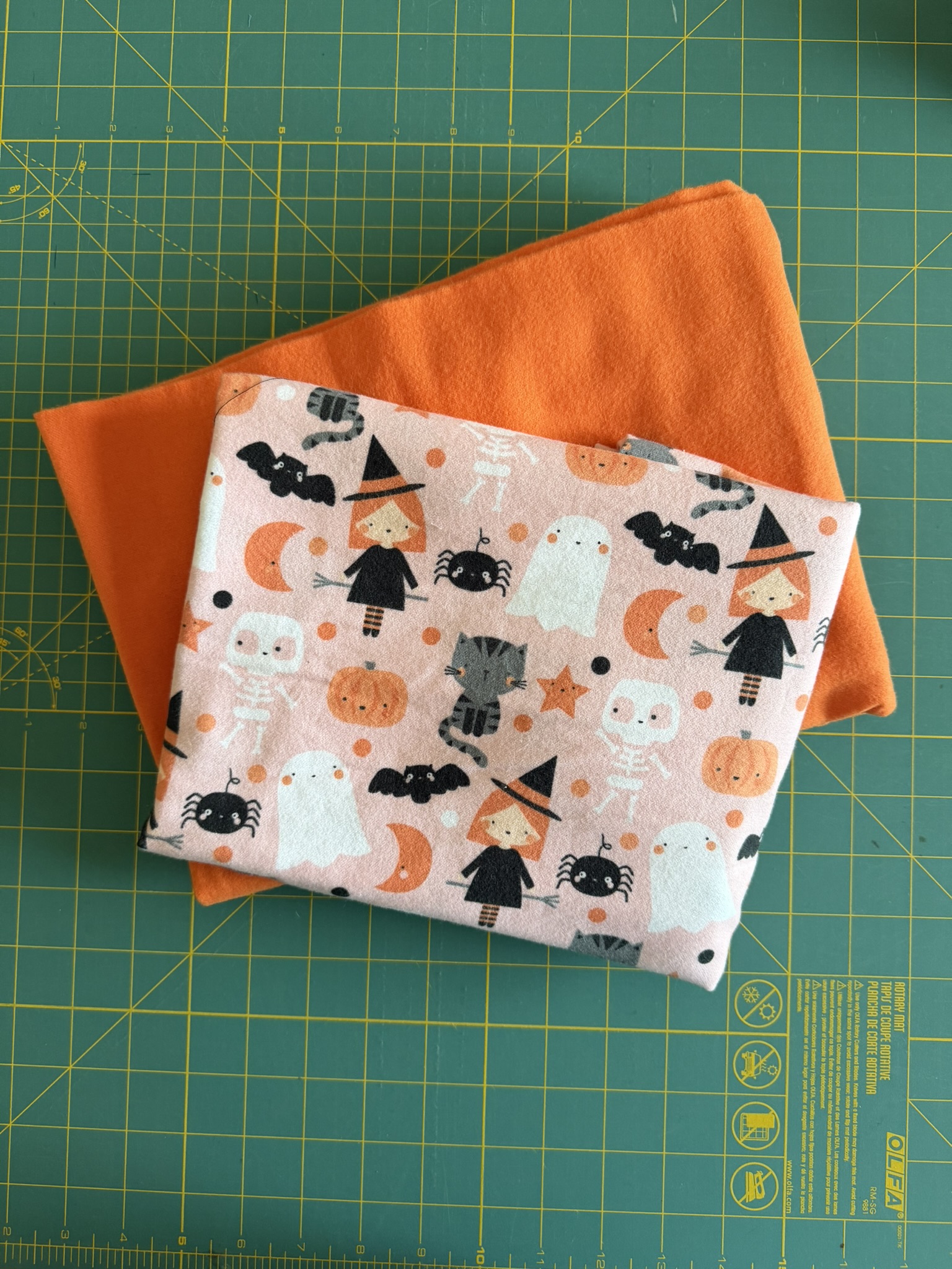 Halloween-themed flannel and orange flannel displayed on a green cutting mat for a toddler pillowcase tutorial.